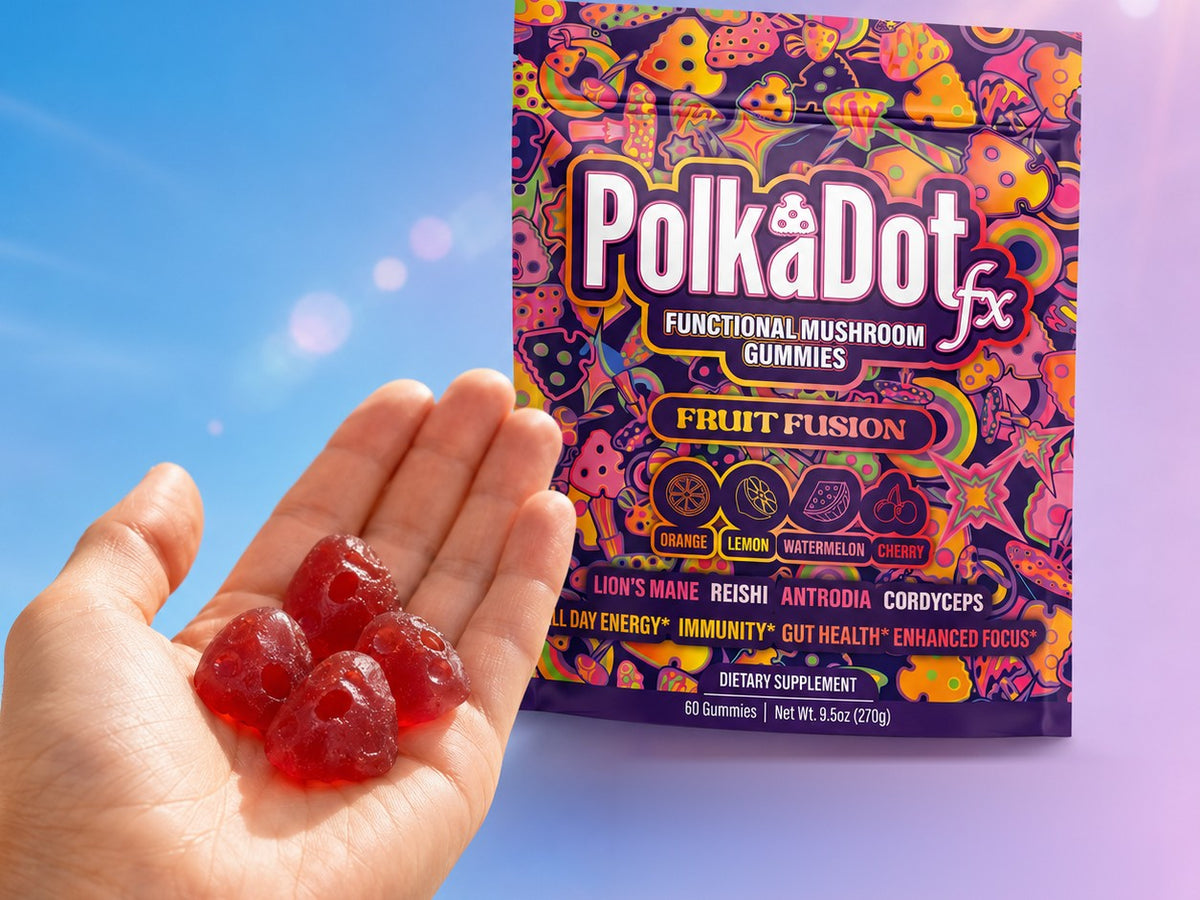 An open hand holding four red PolkaDotFx functional mushroom gummies beside the Fruit Fusion pouch against a blue sky