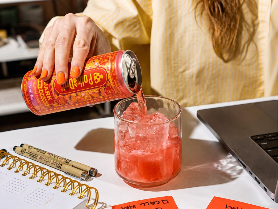 Pouring a Spark Seltzer over ice at a desk beside a planner and laptop